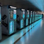 Row of Custom Case Kiosk machines with teal LED lighting in a showroom-style corridor.