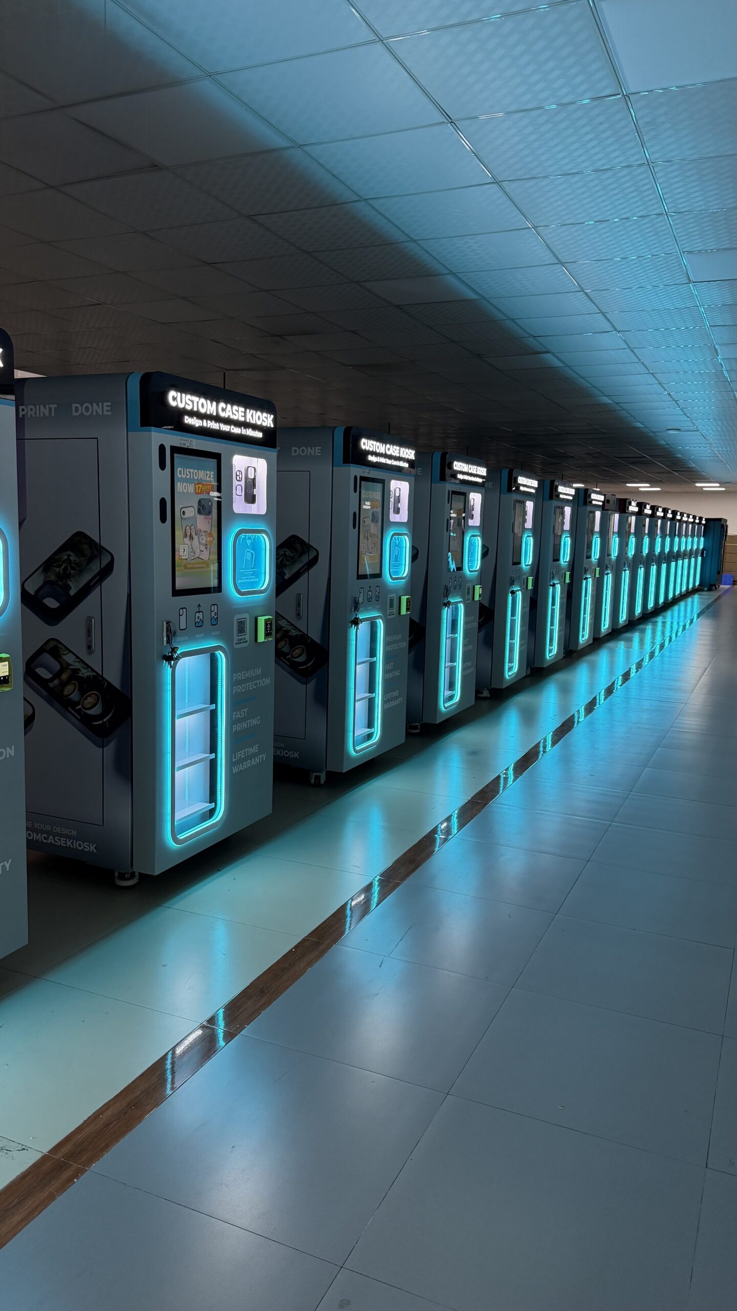 Row of Custom Case Kiosk machines with teal LED lighting in a showroom-style corridor.